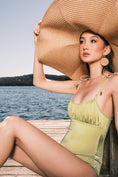 Load image into Gallery viewer, Model wearing Ruched Bust Shoestring One Piece Swimsuit in Green Leaf on a jetty with water in the background